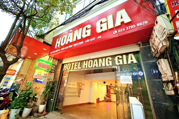 The exterior of Hotel Hoang Gia, featuring a prominent red sign with contact information and a neon sign indicating a nearby hotel. - Hoang Gia Hotel Cau Giay (Hanoi)