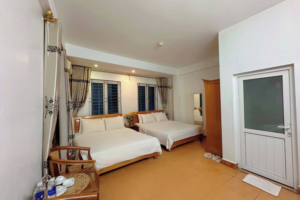 Habitación de hotel con dos camas, una silla de madera, una mesita con artículos de aseo y una puerta con panel de vidrio satinado.