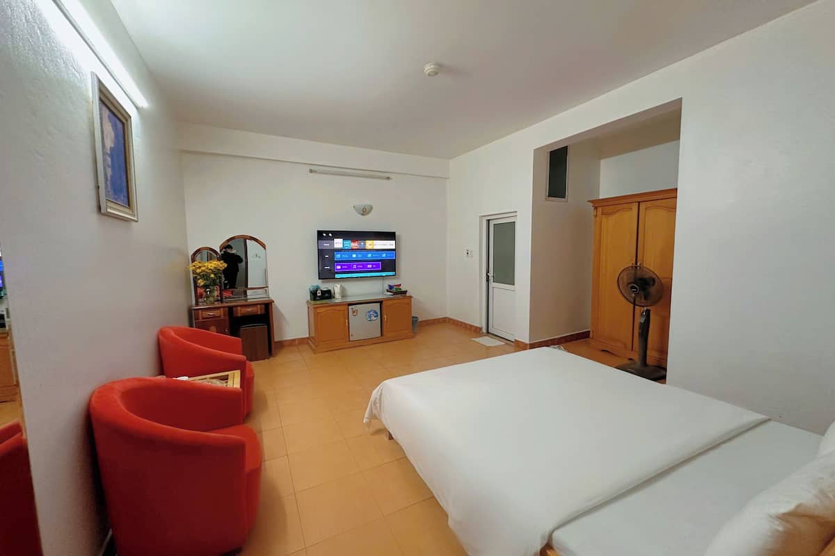 Habitación de hotel con una cama, un escritorio con computadora, televisor y una silla roja.