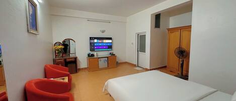 A hotel room with a bed, a desk with a computer, a TV, and a red chair.