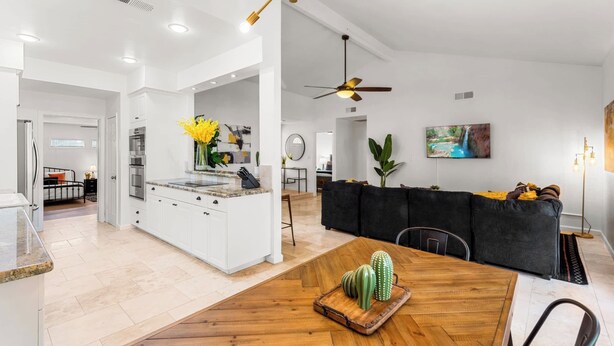 Eine moderne Küche mit weißen Schränken, einem Holzespeisetisch und einem schwarzen Sofa.