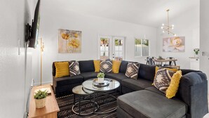 Ein modernes Wohnzimmer mit einem Ecksofa, einem Glastisch und einem Essbereich mit Tisch und Stühlen.