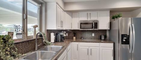 Una cocina moderna con armarios blancos, electrodomésticos de acero inoxidable, encimeras de granito y una ventana con vistas.