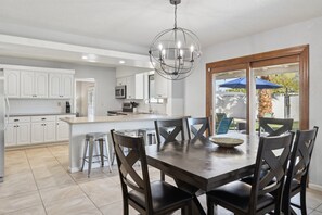 Una cocina moderna con armarios blancos, una isla central y un comedor con mesa y sillas de madera.
