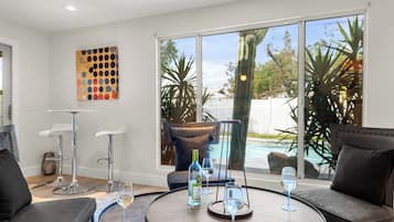 Ein modernes Wohnzimmer mit einem runden Holztisch, zwei Ledersofas, einem großen Fenster mit Blick auf einen Pool und einem farbenfrohen abstrakten Gemälde an der Wand.