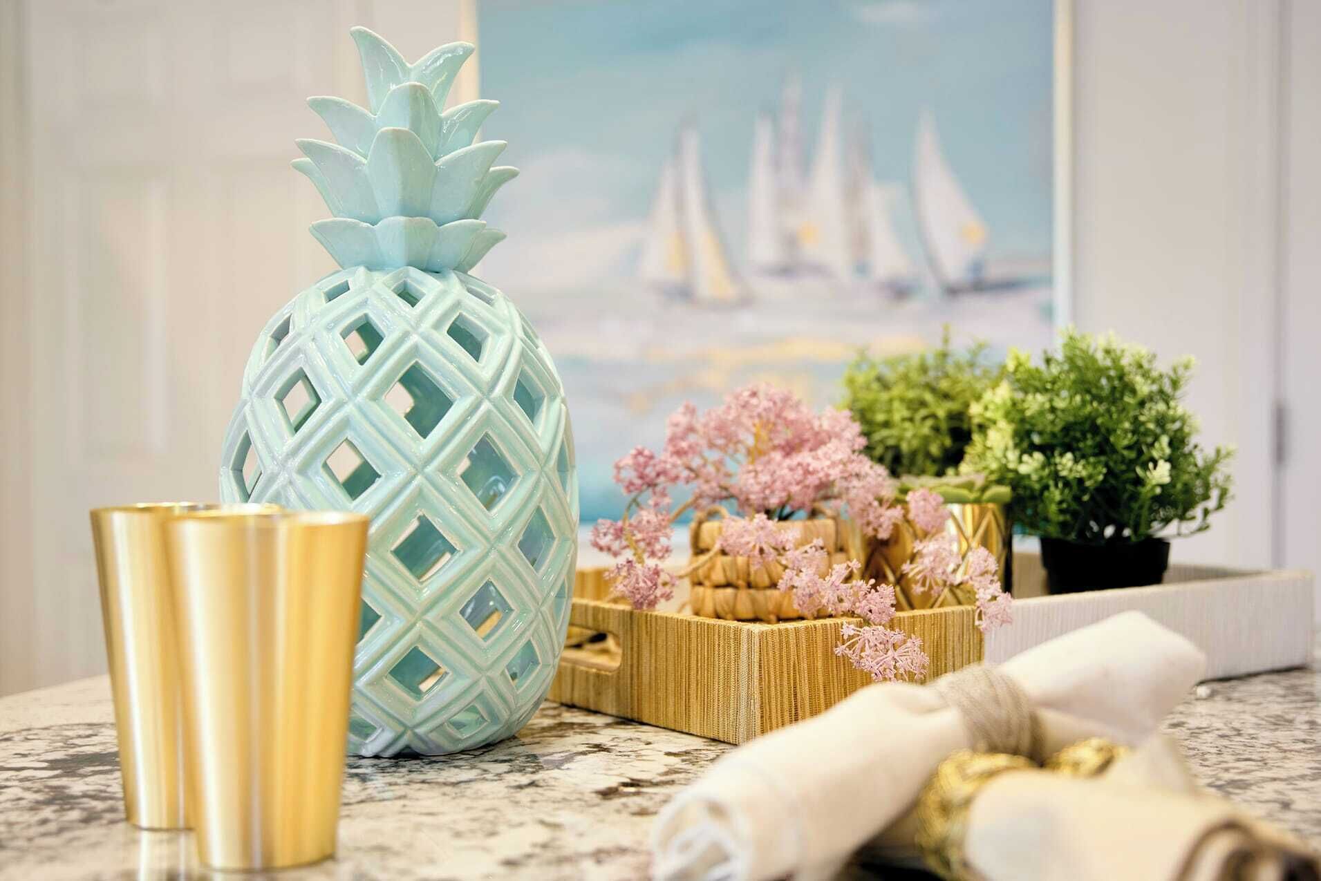A pineapple-shaped vase, a small potted plant, and a decorative box with pink flowers on a countertop.