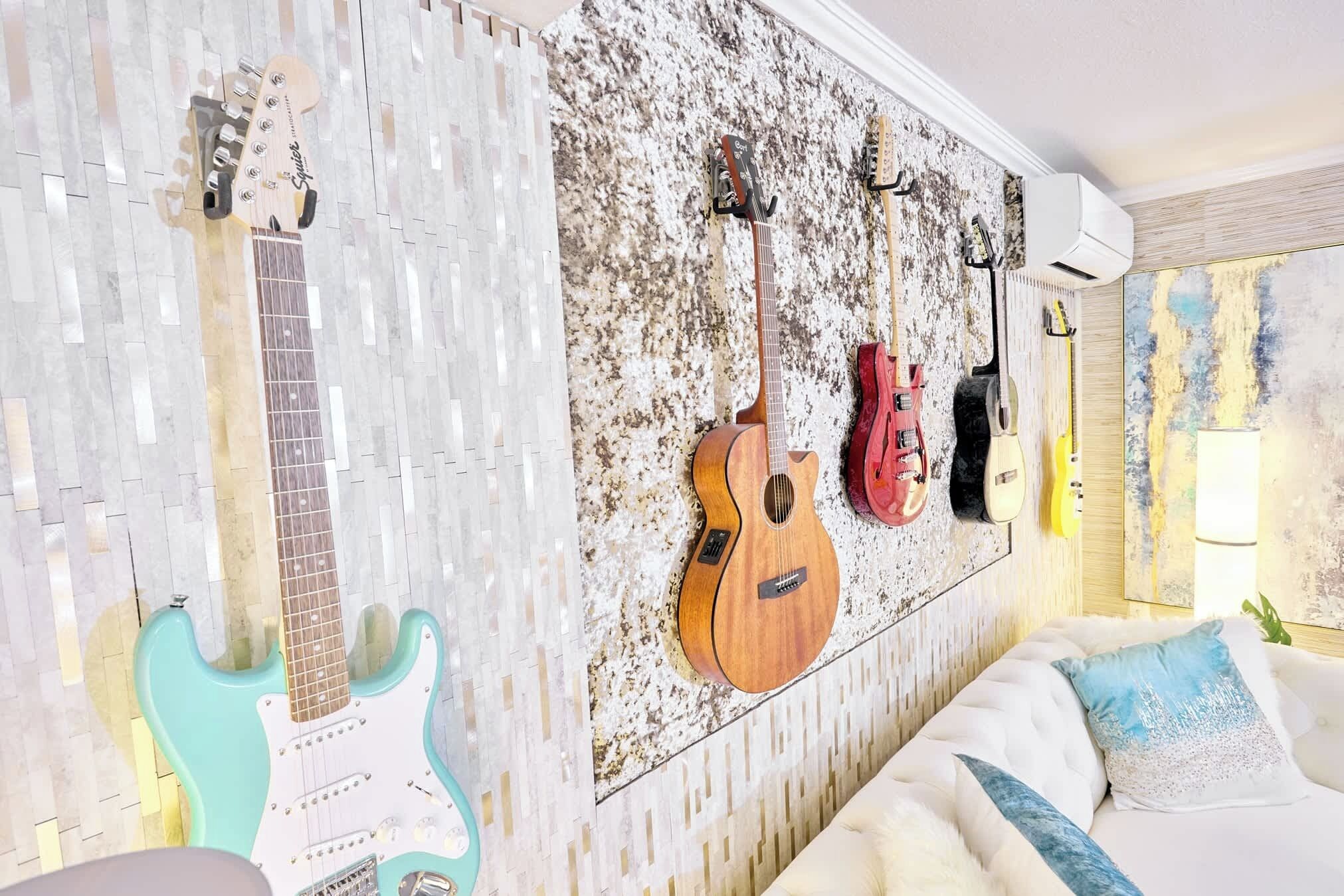 A room with a wall-mounted guitar rack holding three guitars, a white couch with blue pillows, and a textured wall.