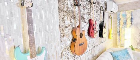 A room with a wall-mounted guitar rack holding three guitars, a white couch with blue pillows, and a textured wall.
