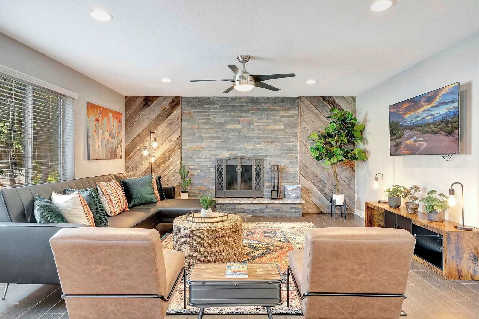 A modern living room with a stone fireplace, a ceiling fan, and a large window.