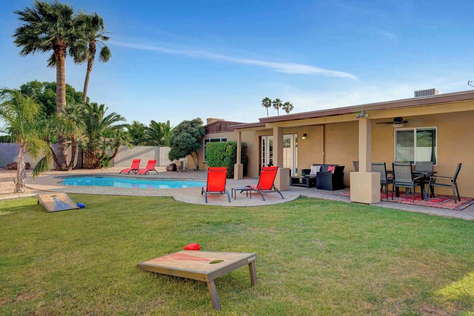 Ein Garten mit Swimmingpool, roten Liegestühlen, einem Essbereich und einem kleinen Tisch.
