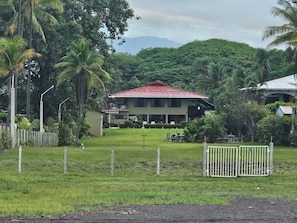 A two-story building with a red roof, surrounded by lush greenery and a fenced yard. - Casa Canadiense Cabina 5 of 5 (Chacarita)