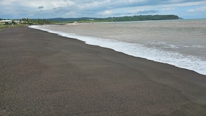 Una spiaggia con una battigia di sabbia scura, mare calmo e cielo nuvoloso.