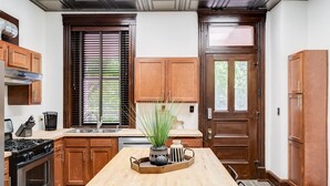 A kitchen with wooden cabinets, a wooden table, a stove, and a window with blinds.