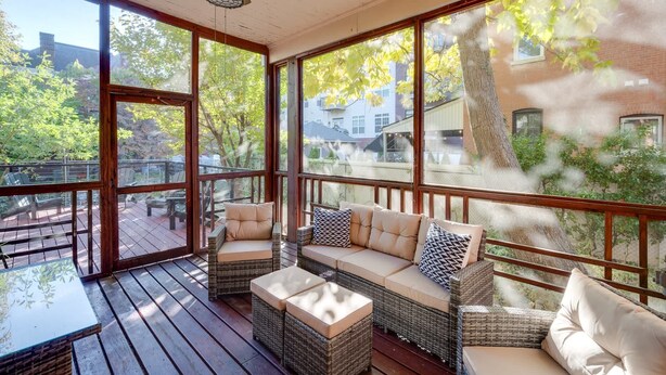 A covered patio with wicker furniture and a table, large windows, and a ceiling fan.