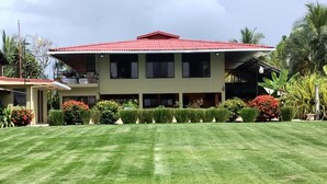 A two-story building with a red roof, surrounded by a well-maintained lawn and various plants. - Casa Canadiense Cabina 1  of 5 BEACHFRONT PROPERTY (Chacarita)