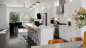 A modern kitchen with white cabinets, a central island, bar stools, and a dining area.