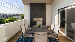 A balcony with a wooden table and chairs, a potted plant, and a view of the cityscape.