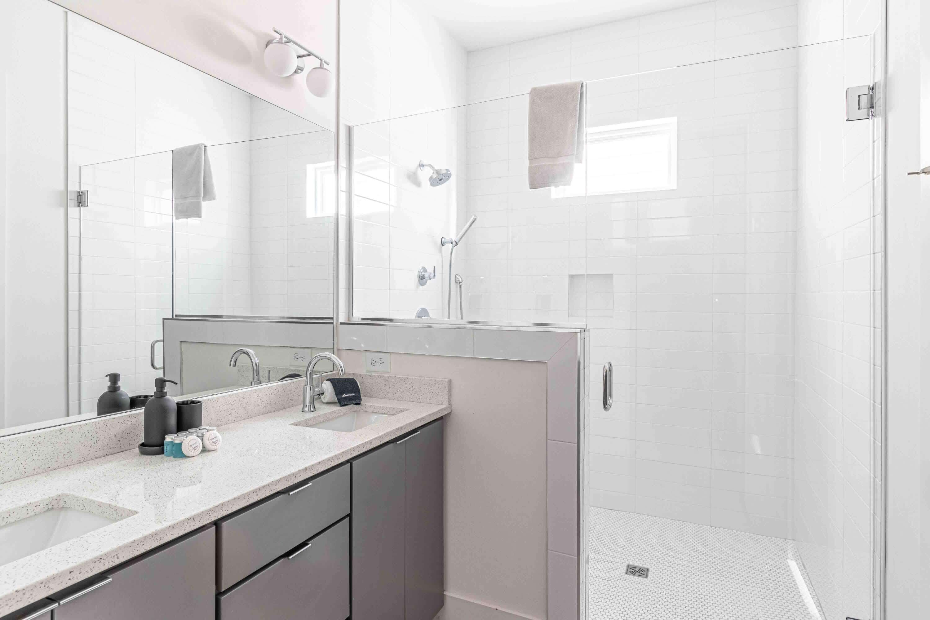 Et moderne badeværelse med en brusekabine i glas, et stort spejl og en bordplade med toiletartikler.