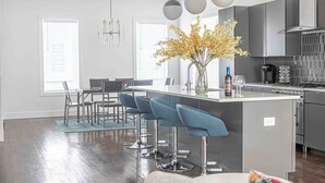 Una cocina moderna con una isla central, taburetes de bar y un comedor con mesa y sillas.