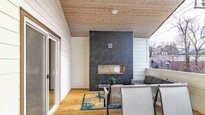 Un patio techado con piso de madera, puerta corrediza de vidrio, chimenea y mobiliario exterior.