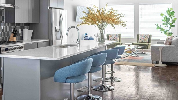 Una cocina moderna con una isla central, taburetes de bar y un comedor con sofá y sillas.