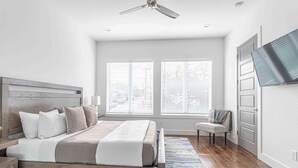 Un dormitorio con cama, una silla, un televisor y un ventilador de techo.