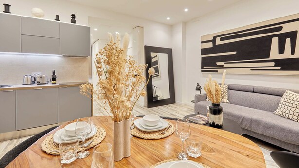 A modern living room with a grey sofa, a dining table set with plates and glasses, and a kitchen area with cabinets and appliances. - Superb Apartment Invalides St Germain des Pres (Paris)