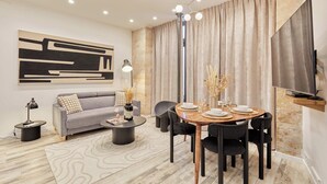 A modern living room with a sofa, coffee table, dining table, and chairs. There is a TV mounted on the wall and a large abstract painting above the sofa. - Superb Apartment Invalides St Germain des Pres (Paris)