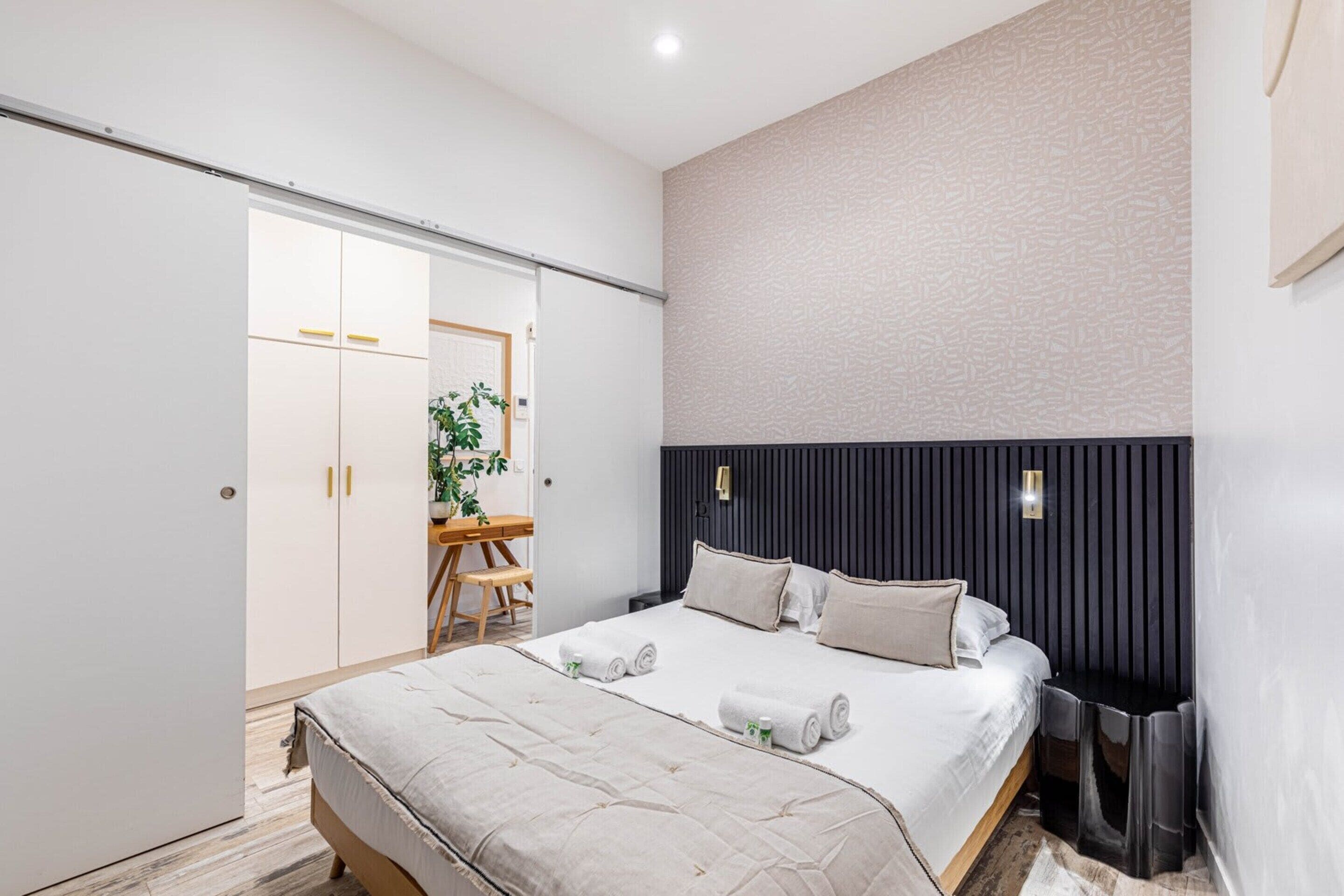 A modern bedroom with a bed, bedside tables, a wardrobe, and a desk with a chair.