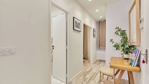 A hallway with a wooden floor, a small wooden stool, a potted plant, and framed pictures on the wall. - Superb Apartment Invalides St Germain des Pres (Paris)