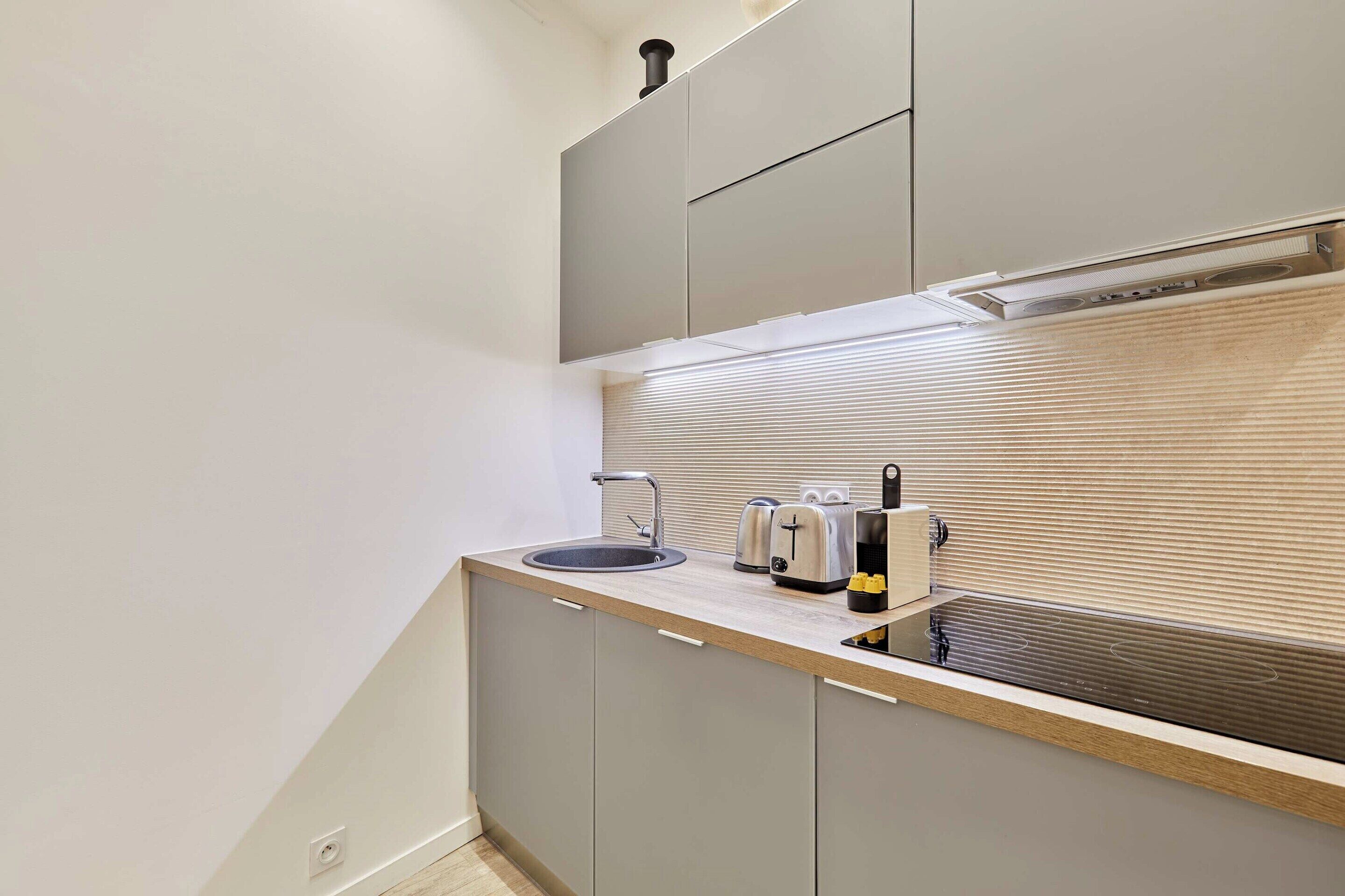 A compact kitchen with a sink, toaster, and cabinets.