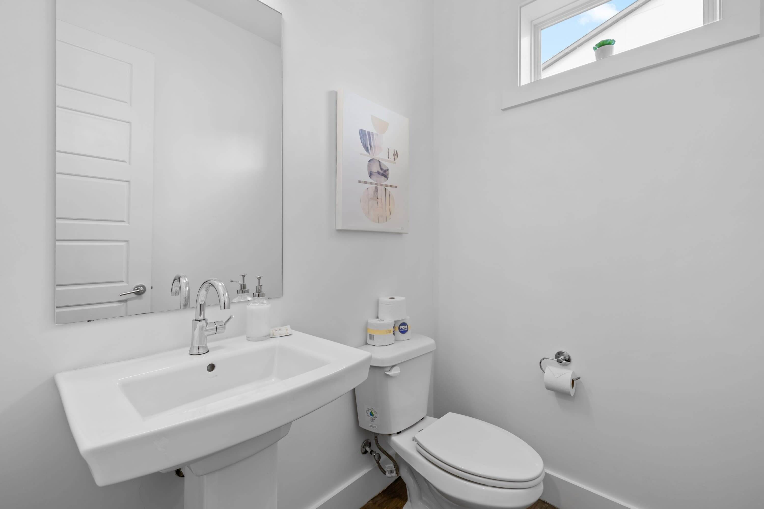 Un baño con lavamanos blanco, inodoro y ventana con planta.