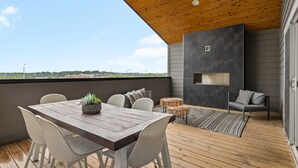 A wooden deck with a dining table and chairs, a seating area with cushions, and a built-in fireplace.