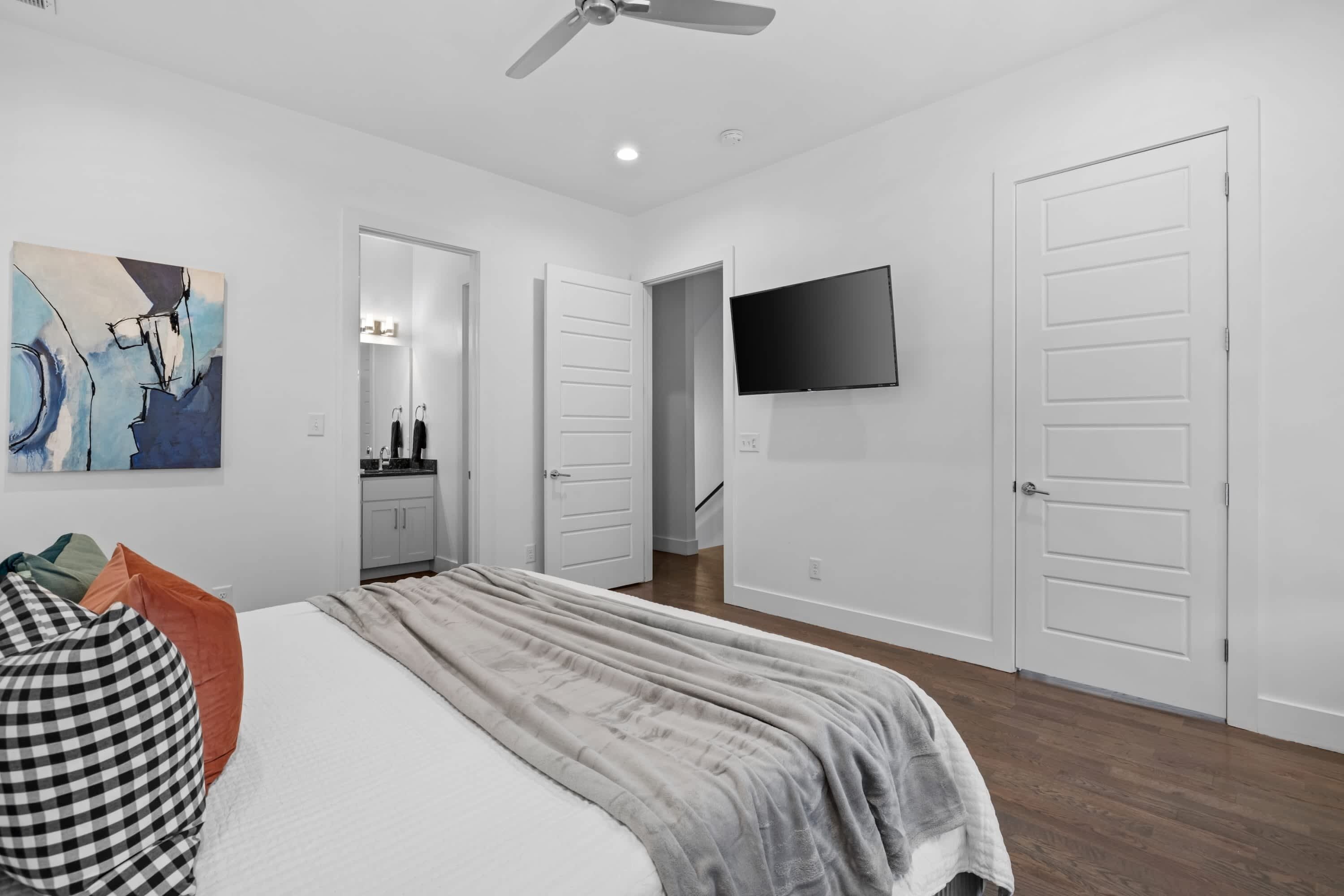 Une chambre à coucher moderne avec un lit, un ventilateur de plafond, un téléviseur à écran plat et un tableau au mur.