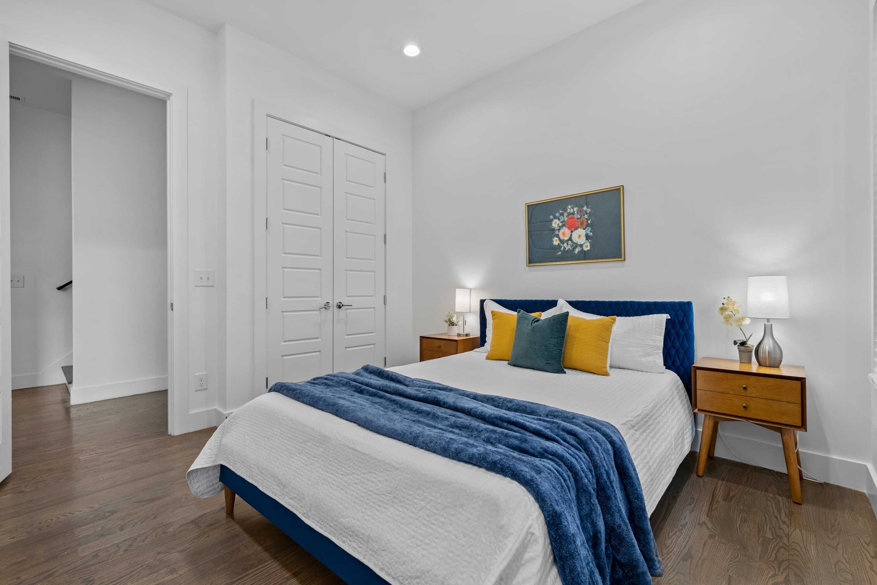 A bedroom with a bed, nightstands, a painting, and a door.