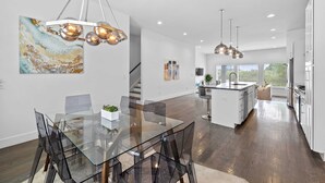 A modern kitchen with a glass dining table, stainless steel appliances, and pendant lighting.