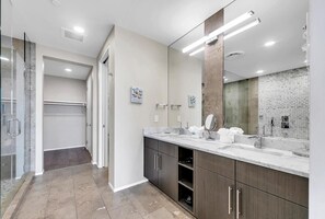 Un baño moderno con un espejo grande, dos lavamanos y una ducha a ras de suelo.