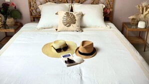 A bedroom with a decorative headboard, a bed with white bedding, a hat, sunglasses, and a magazine on the bed. - La Résidence Belle Créole (Quincy-Voisins)