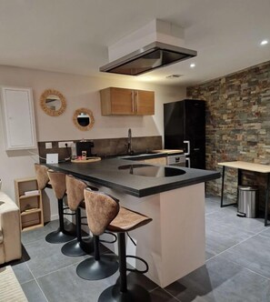A modern kitchen with a central island, bar stools, a built-in oven, and a stone accent wall. - La Résidence Belle Créole (Quincy-Voisins)