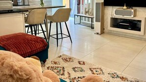 A modern living room with a sofa, a TV, and a kitchen area in the background. - La Résidence Belle Créole (Quincy-Voisins)