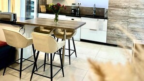 A modern kitchen with a central island, a dining area with two chairs, and a view of the living room. - La Résidence Belle Créole (Quincy-Voisins)