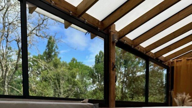 A hot tub with clear water, surrounded by a wooden pergola and large windows overlooking trees. - La Résidence Belle Créole (Quincy-Voisins)