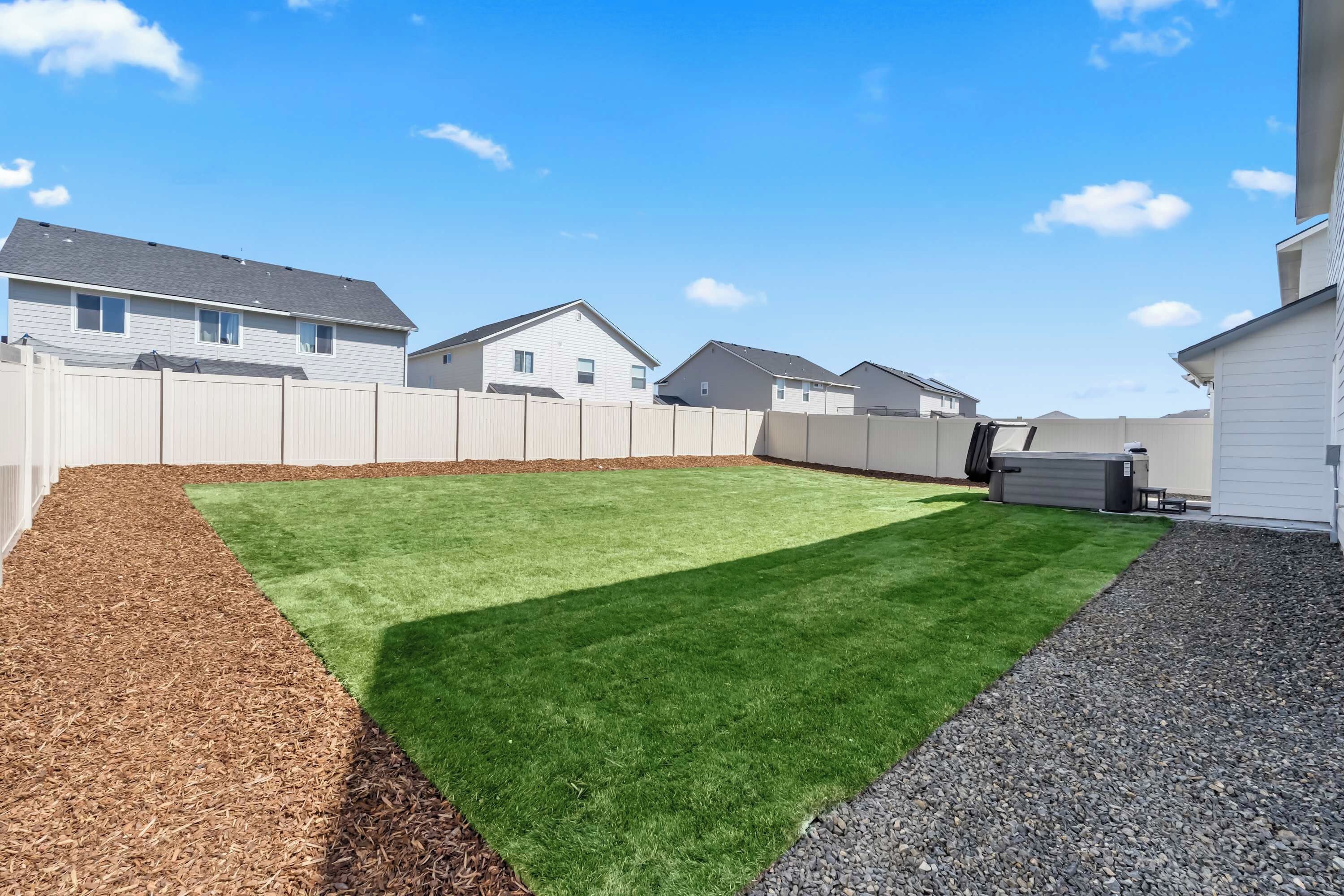 A backyard with a green lawn, a wooden fence, and a gravel path.
