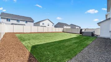 A backyard with a green lawn, a wooden fence, and a gravel path.