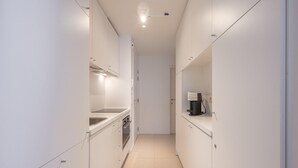A narrow, modern kitchen with white cabinetry, a stainless steel sink, and a coffee machine on the countertop. - Apartment in Heist Near the Beach (Knokke-Heist)