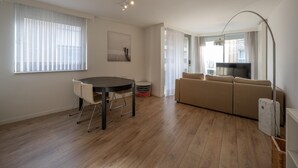 A modern living room with a round dining table, a sofa, and a TV. - Apartment in Heist Near the Beach (Knokke-Heist)