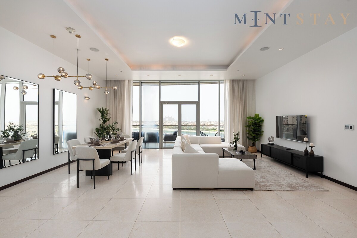 A modern living room with a white sofa, dining table, chairs, and a large window with a view.