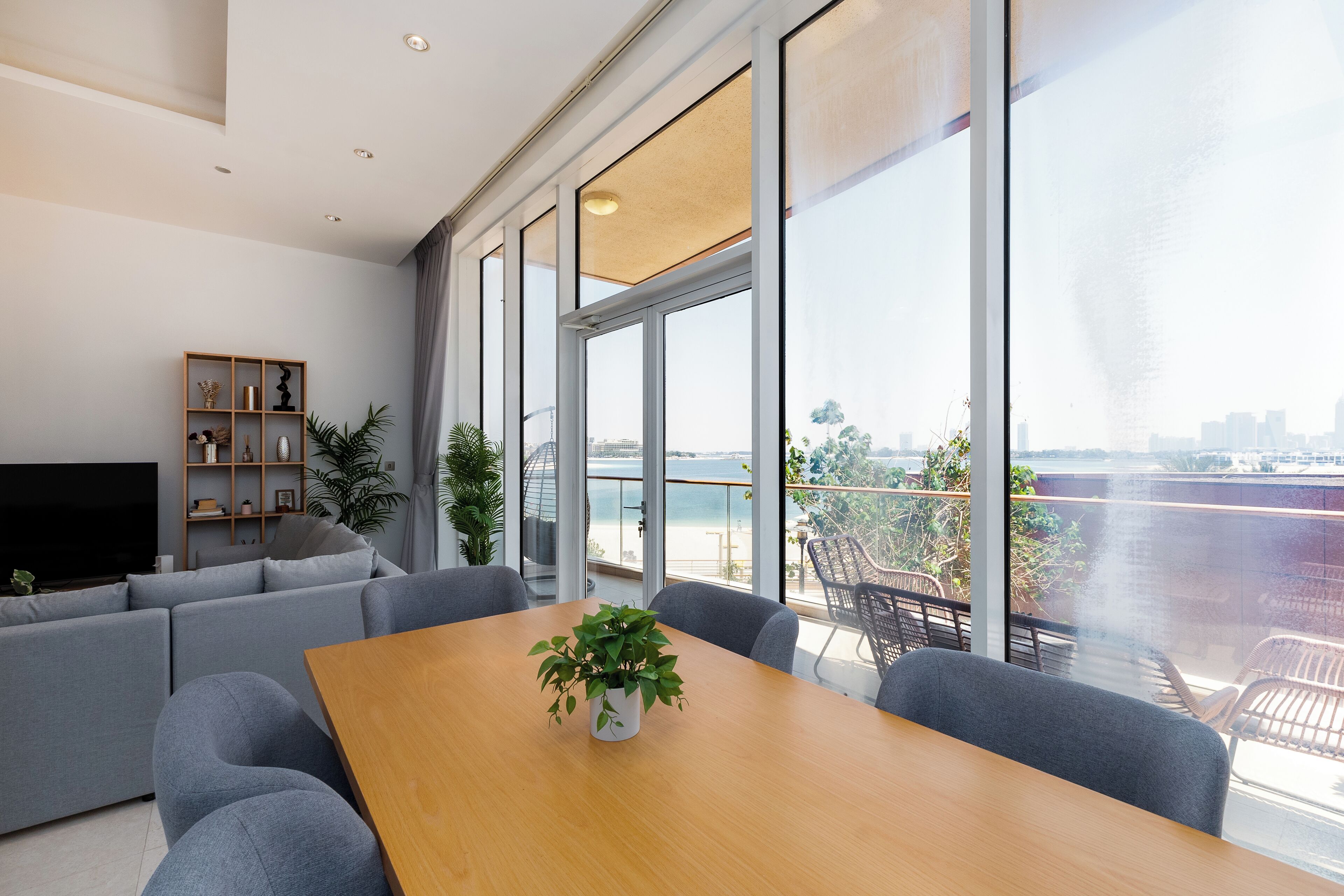 Een moderne woonkamer met een groot raam, een grijze bank, een houten tafel en een televisie.