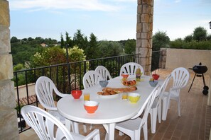 A round white table with chairs, a basket of bread, and bowls of fruit and juice. - Le Jardin De Lucette (Le Rouret)