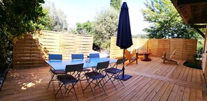 A wooden deck with a table and chairs, surrounded by a wooden fence and trees. - Le Jardin De Lucette (Le Rouret)